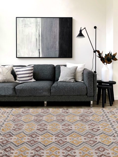 Monivärinen, kuvioitu, käsinkudottu Kiara-villamatto olohuoneen lattialla keskilattiamattona sohvan edessä.