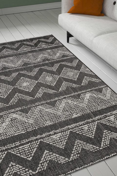 Tummanharmaa, inkatyyliin kuvioitu Modena Inka-matto olohuoneen lattialla.